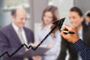 A blurred photo of people in an office, overlapped by a hand drawing a black line chart.