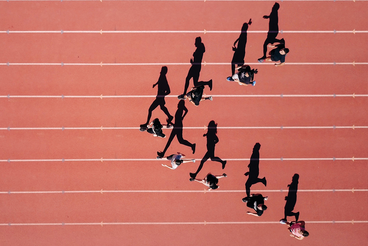 Birdseye photo of 8 runners on a track with their shadows stretching out.