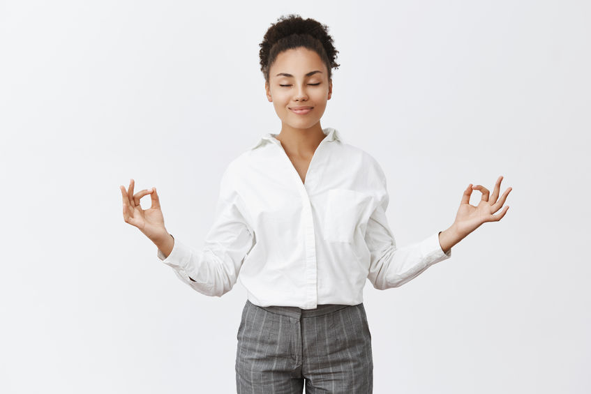 A woman in business casual dress meditating while standing up.