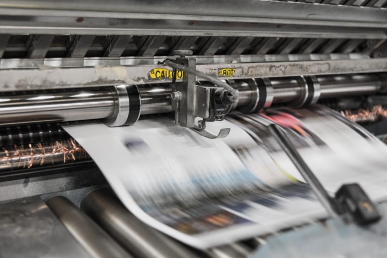 A printing press is printing colored newspapers.