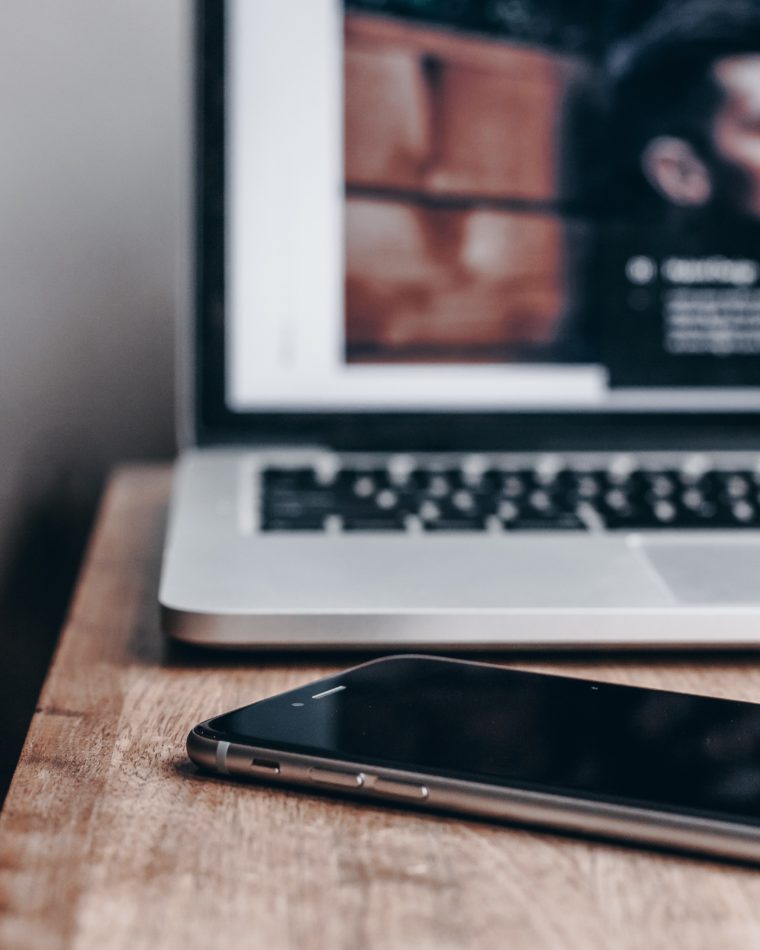 An iPhone and laptop on a wooden desk.