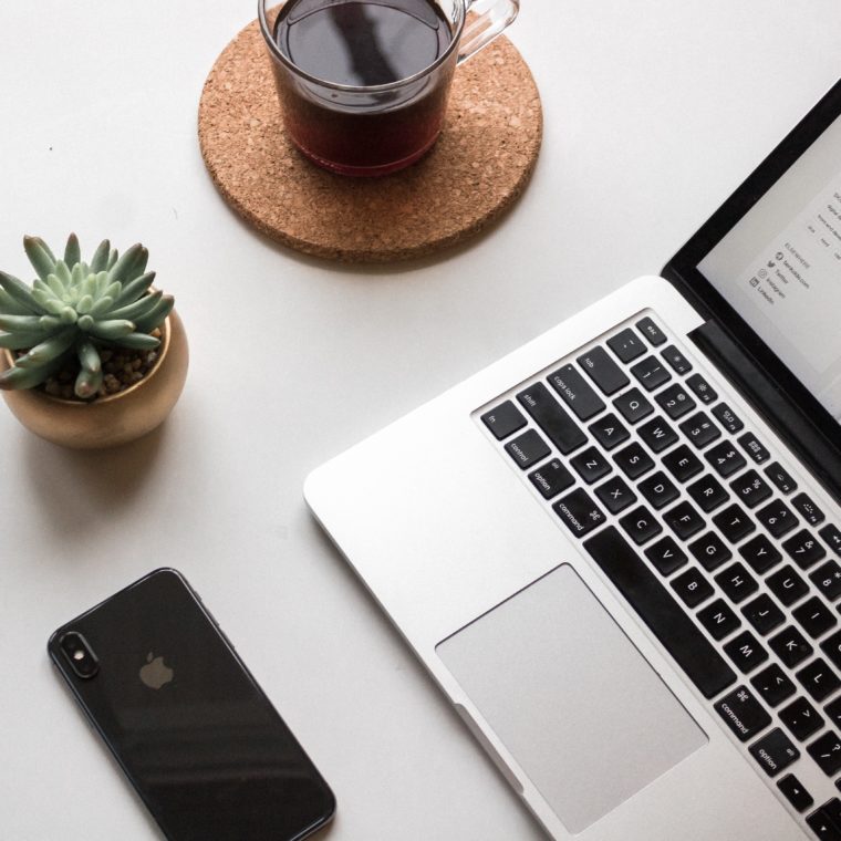 A desk with a laptop, phone, cup of coffee, and a succulent.