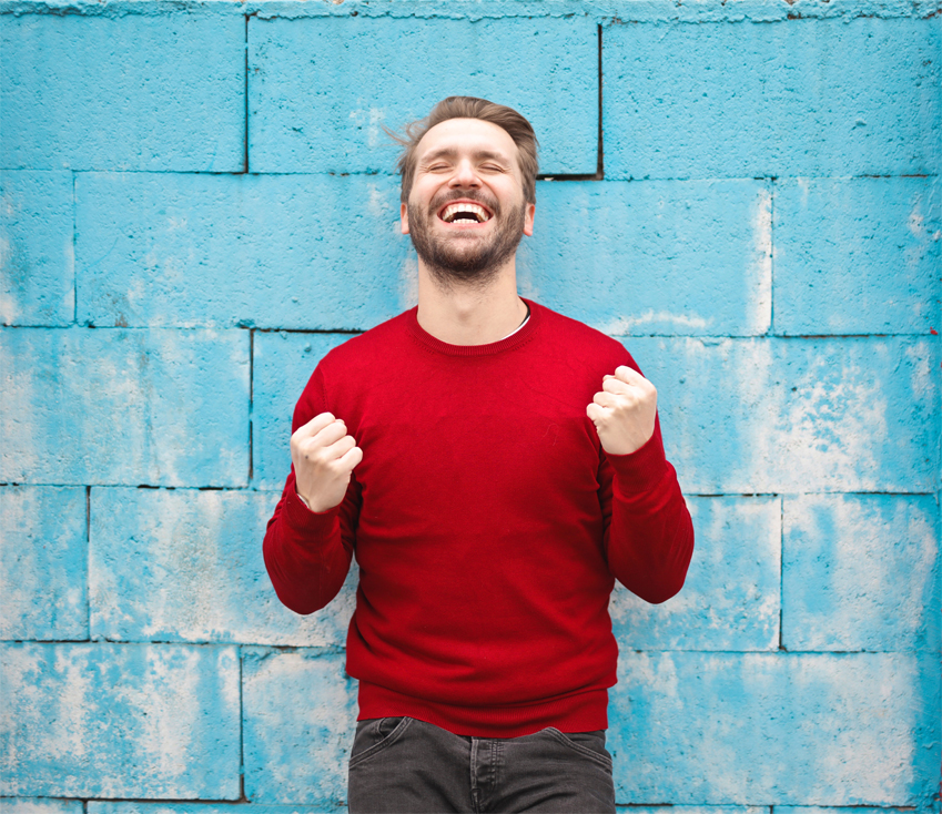 A joyful man in a red sweater looking very excited in front of a blue wall.