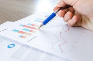 A person marking up a bar graph and line chart with a blue pen.