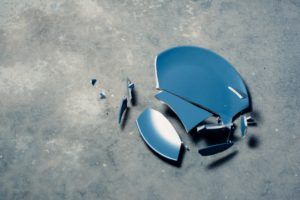 A dark blue dinner plate is shattered on a concrete floor.