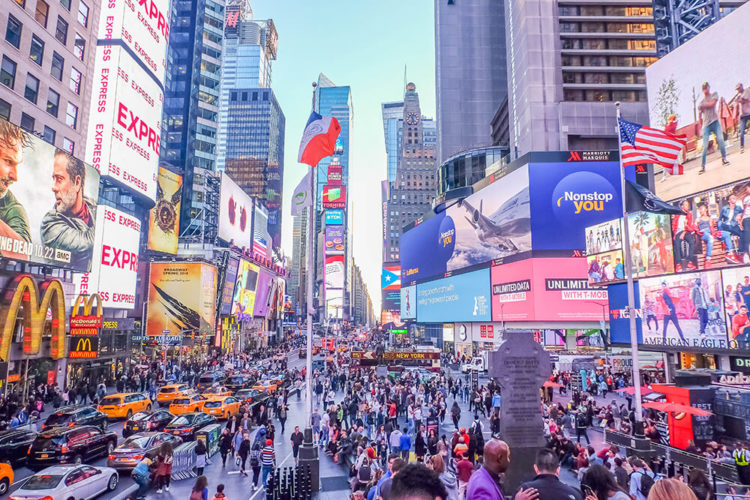 An image of Times Square with big electronic billboards, traffic, and a large crowd.