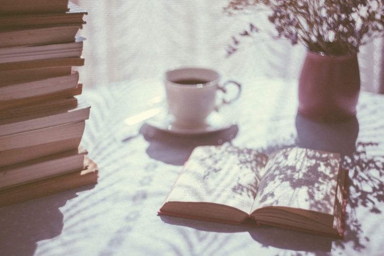 A vintage style photo of a stack of books, a cup of coffee, and a vase with flowers.