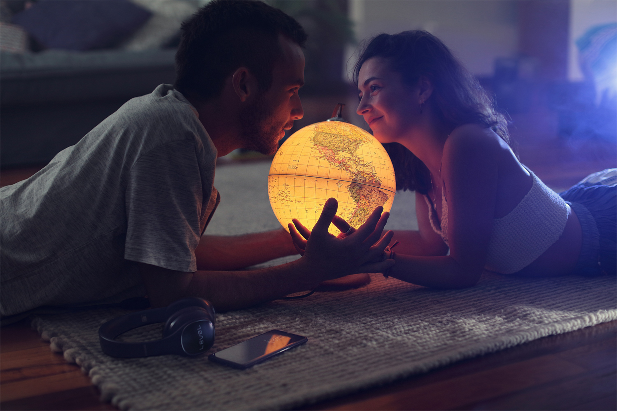 A smiling couple laying on the floor holding a glowing globe.