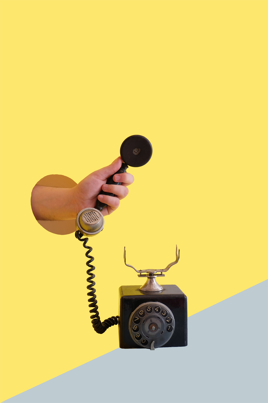 A rotary phone being held in a person's hand. The hand is emerging from a cutout in the wall.