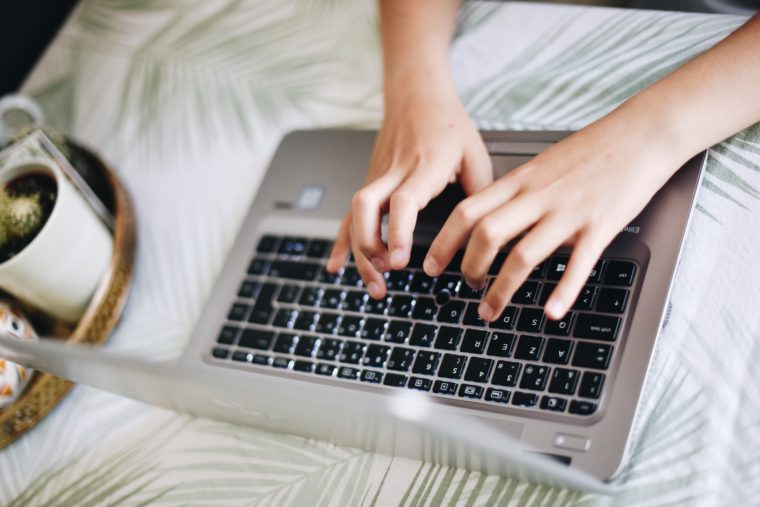 A person's hands are typing on a laptop. The desk has a palm frond pattern and a cup of coffee.