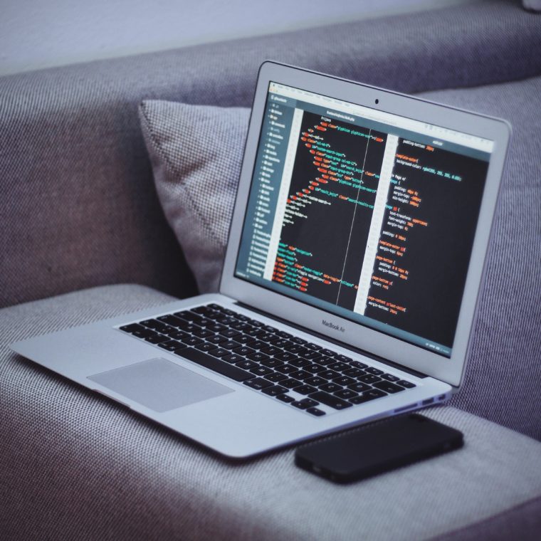 A Macbook Air balanced on a couch with a phone. The screen displays computer code.