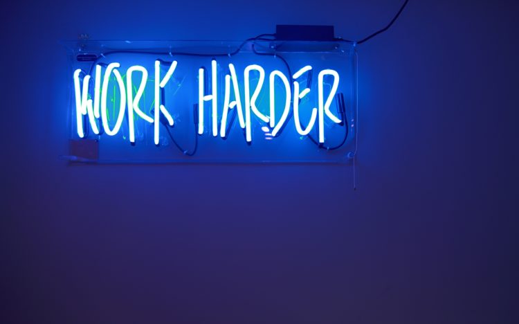 A blue neon sign that reads, "Work Harder".