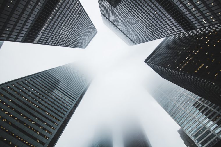 Skyscrapers as seen from the street looking up. Shiny black buildings disappear into a cloudy sky.