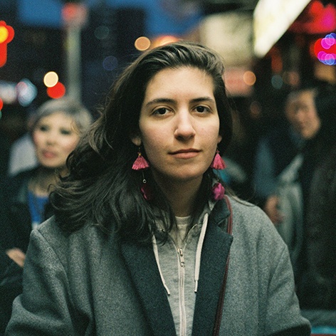 Photo of Lauren McCracken. She is on a busy city sidewalk. She wears pink earrings and grey jacket.