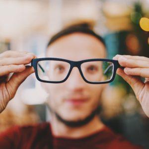 A person holding out their glasses from their face.