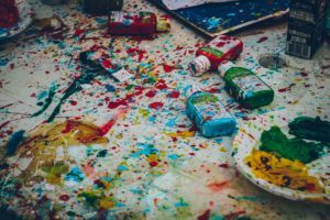 A floor covered in splattered paint, paint containers, and palettes.