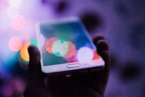A person holding a smartphone with multicolored bokeh lights reflecting off the screen.