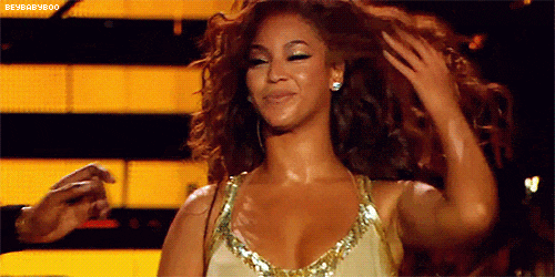A GIF of Beyonce in a gold dress, flipping her hair and winking.