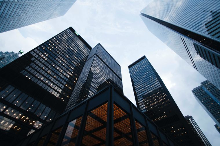 Skyscrapers as seen from the street looking up. Shiny black buildings are against a cloudy sky.