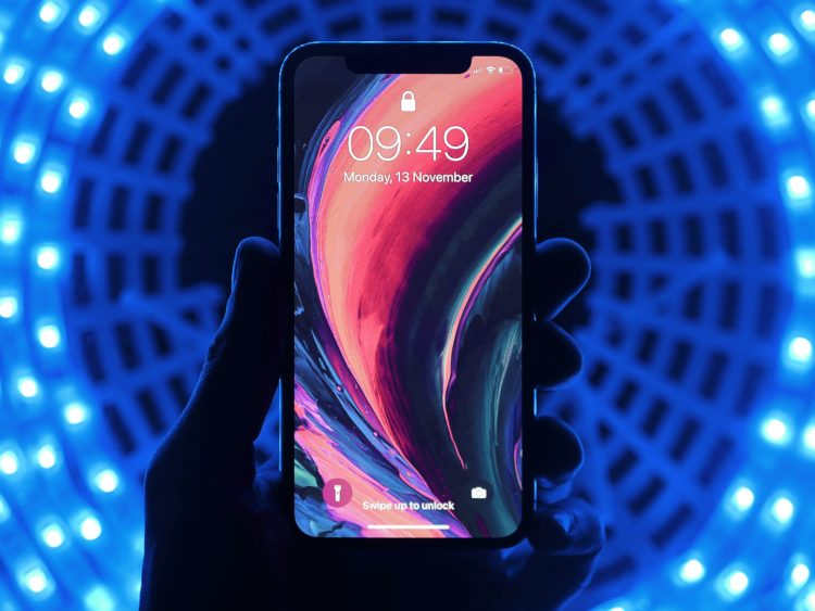 A hand holding an iPhone with a psychedelic background. The person is in a tunnel lit up in blue.