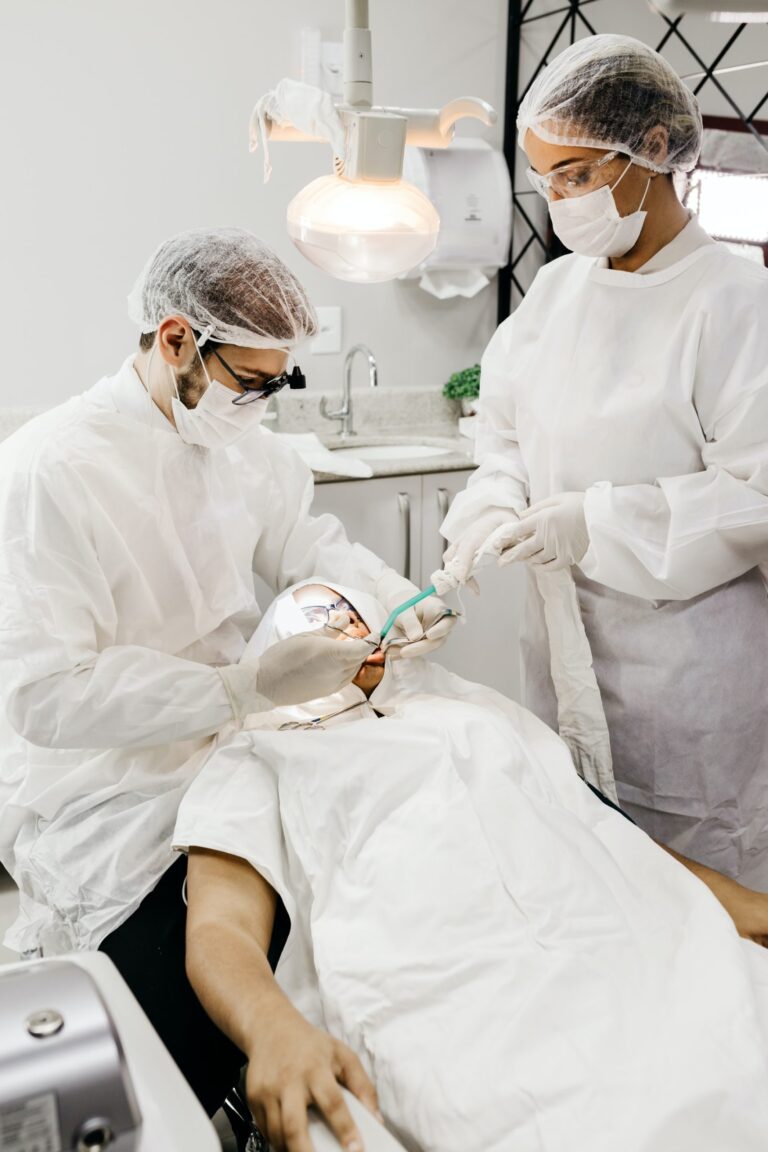 A dentist and a dental assistant wearing white scrubs examine a patient in the dentist's chair.
