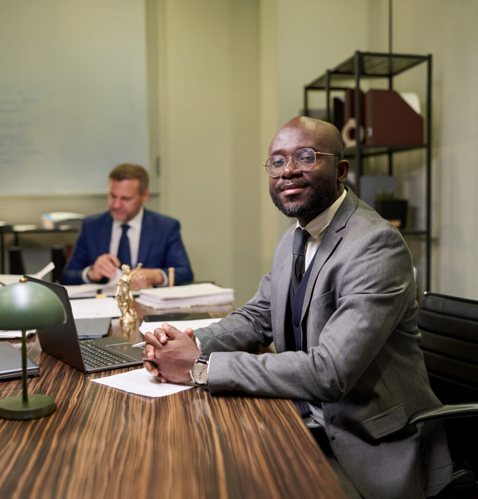 Portrait Of Young Adult Black Lawyer Smiling Confidently While Sitting At Desk