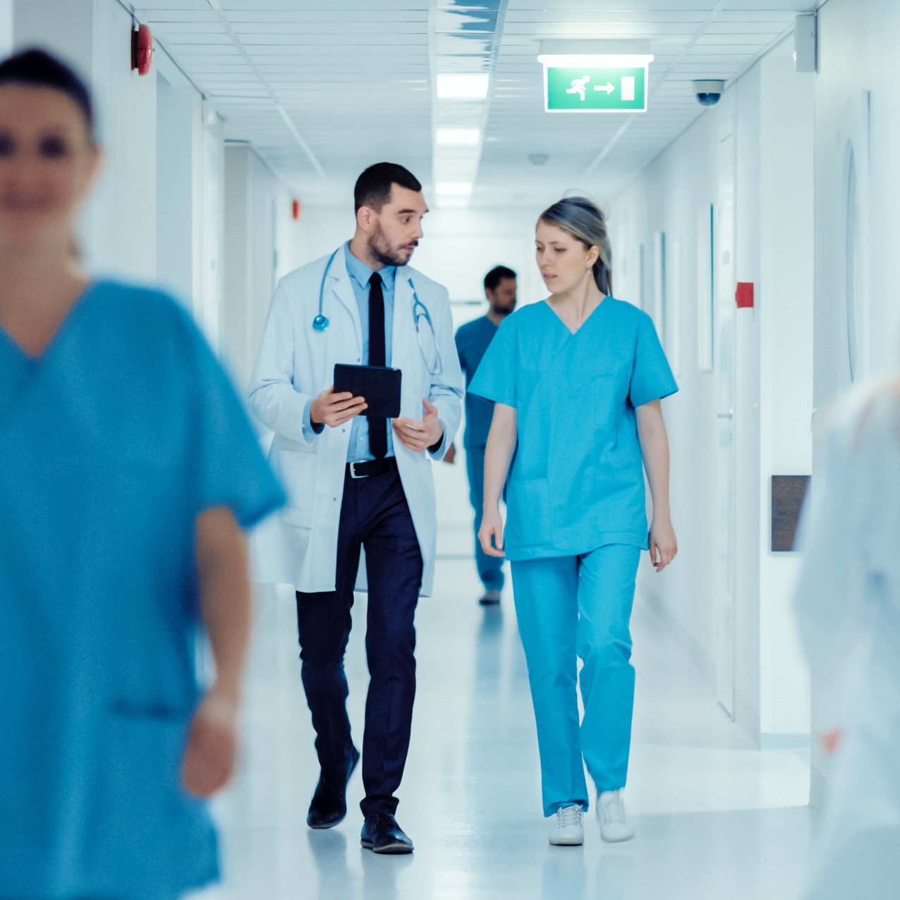 Surgeon And Female Doctor Walk Through Hospital Hallway